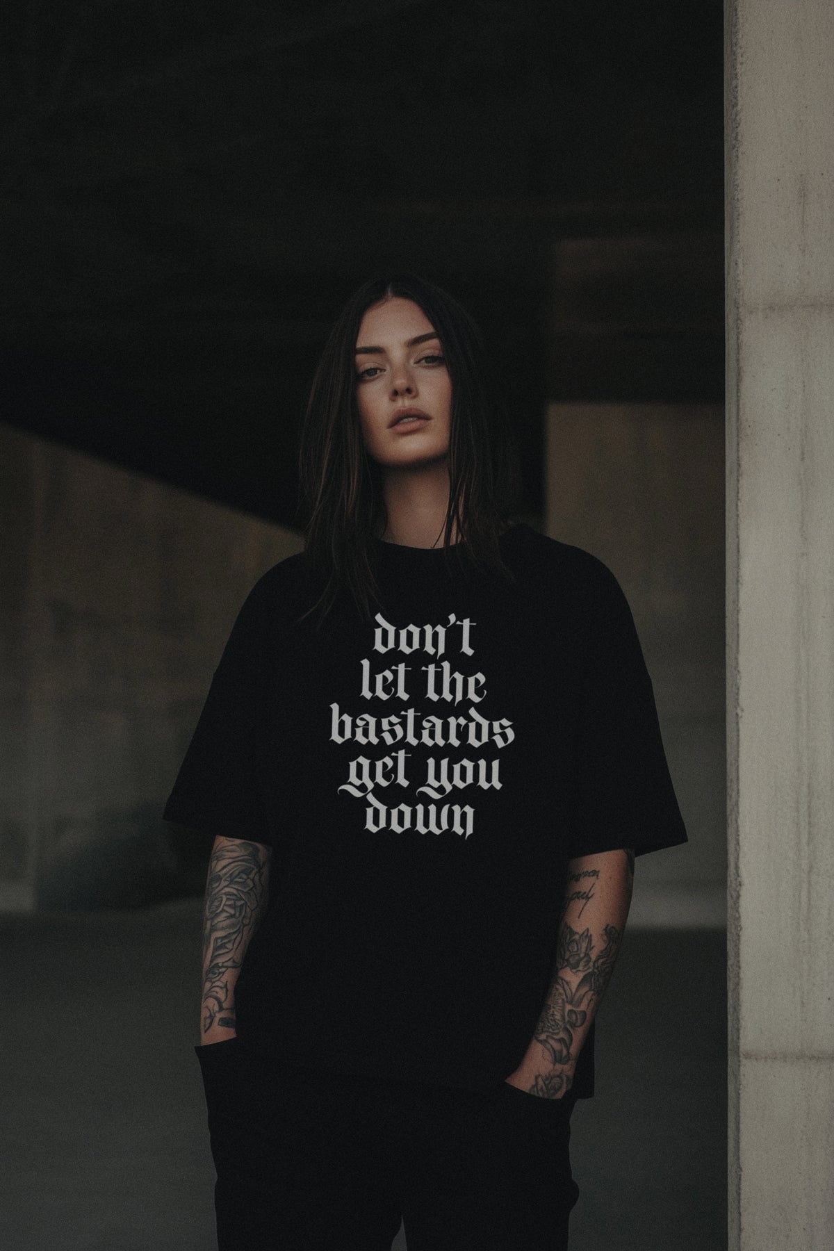 Person wearing a black t-shirt with the text Don't Let the Bastards Get You Down written in a gothic font on a dark background