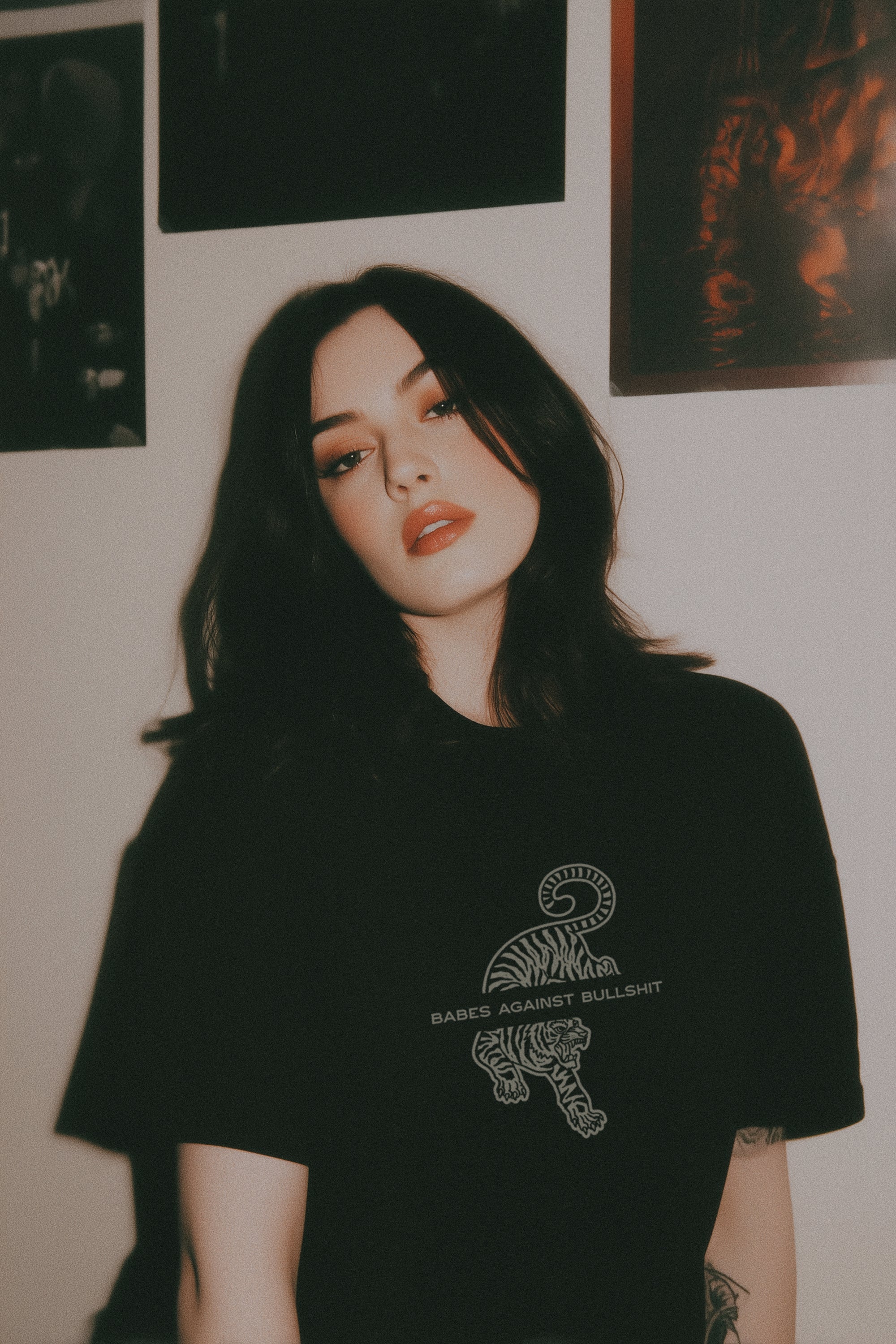 Person wearing a black t-shirt with a graphic design against a wall with posters.