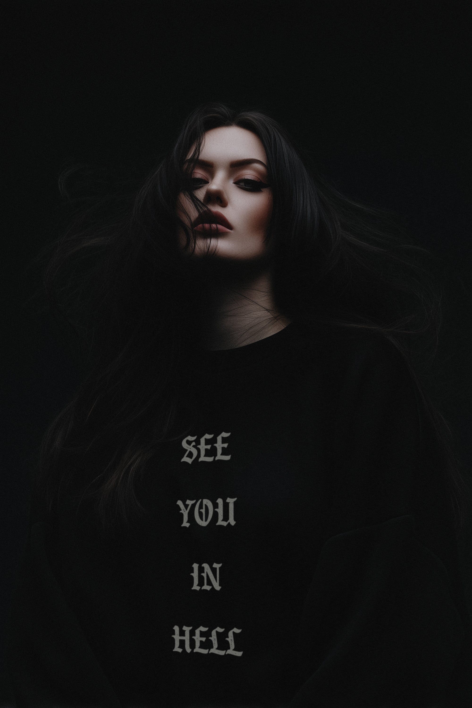 Person wearing a black shirt with 'SEE YOU IN HELL' text against a dark background