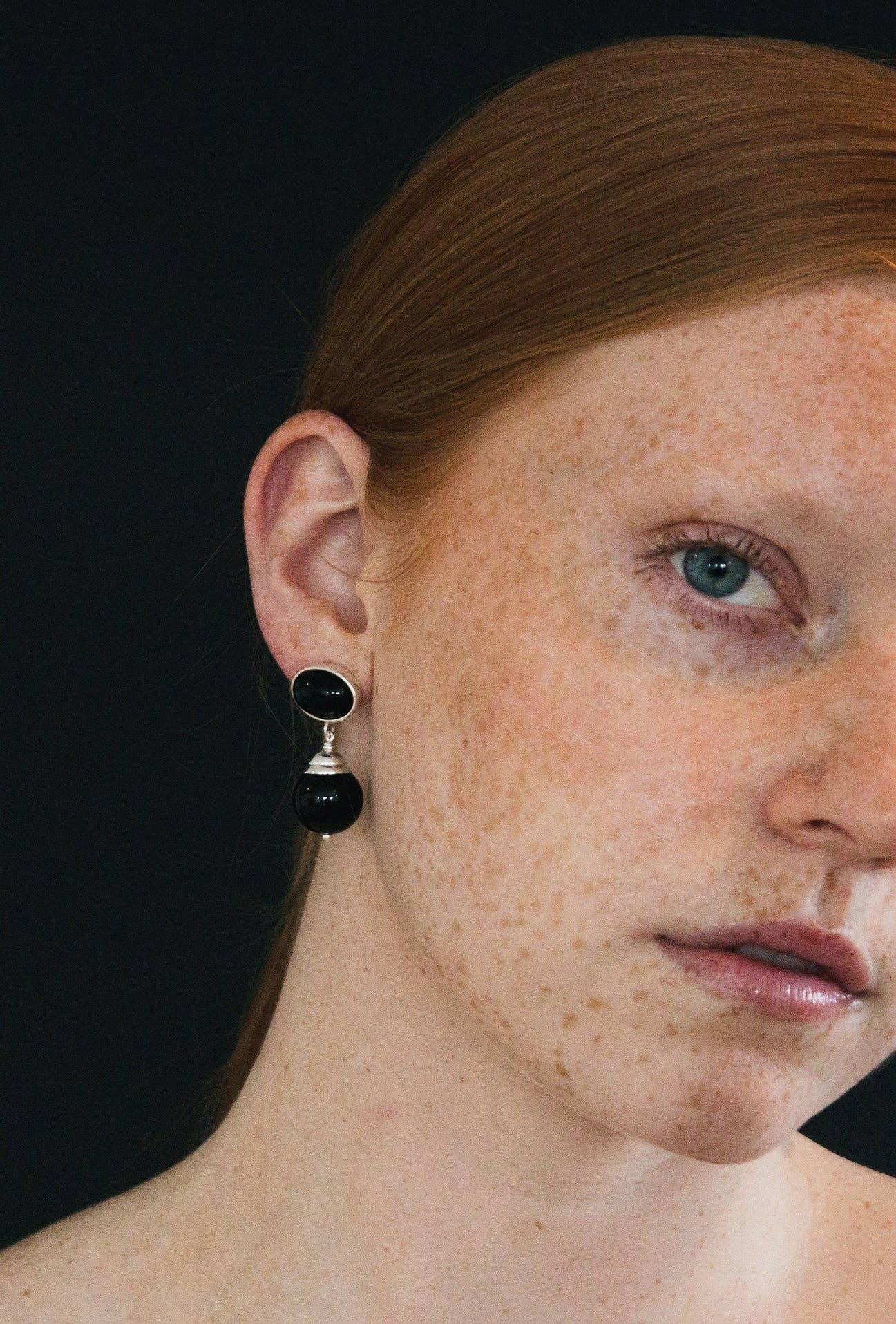 Close-up of a person wearing black earrings with a dark background