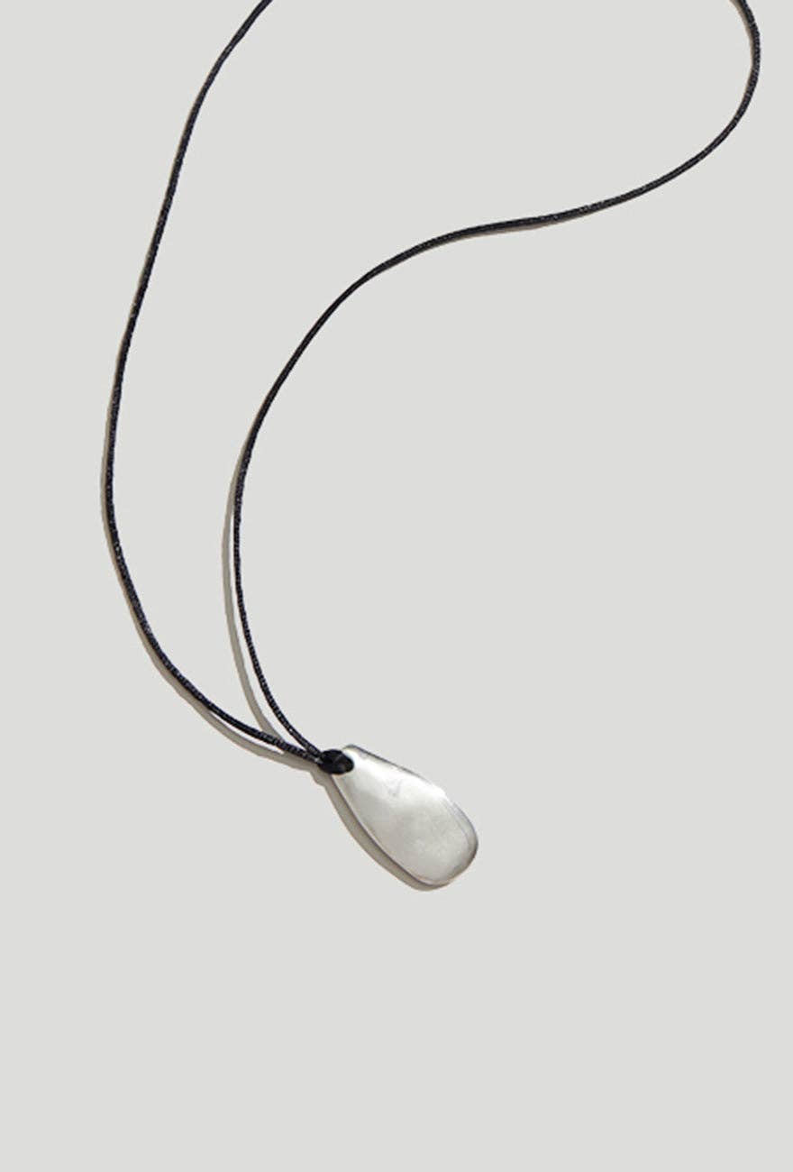 Silver pendant necklace on a thin black cord against a light gray background