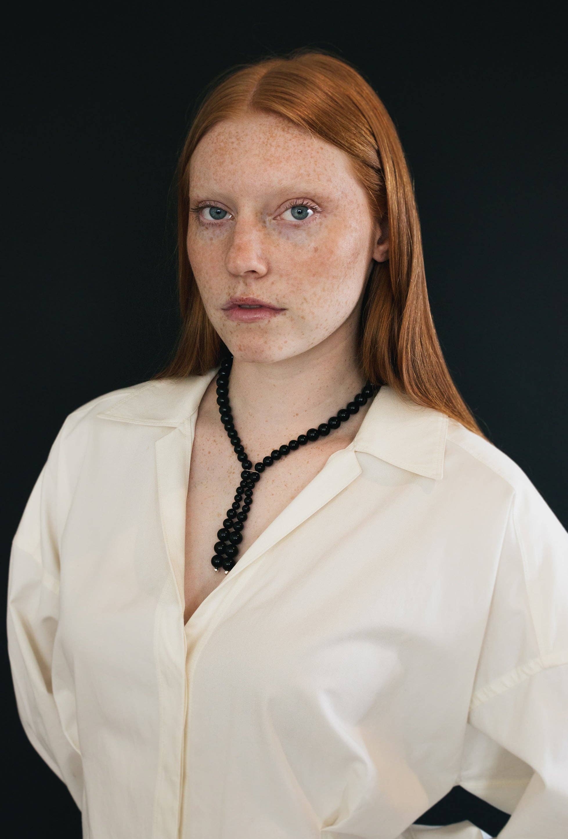 Woman wearing a white blouse and black necklace against a black background