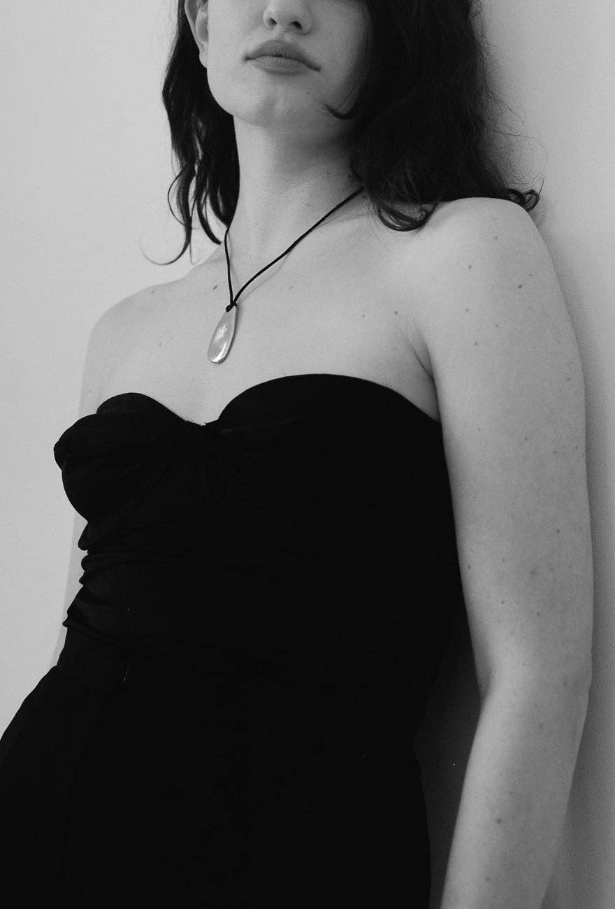 Black and white photo of a person wearing a strapless dress and necklace against a plain background