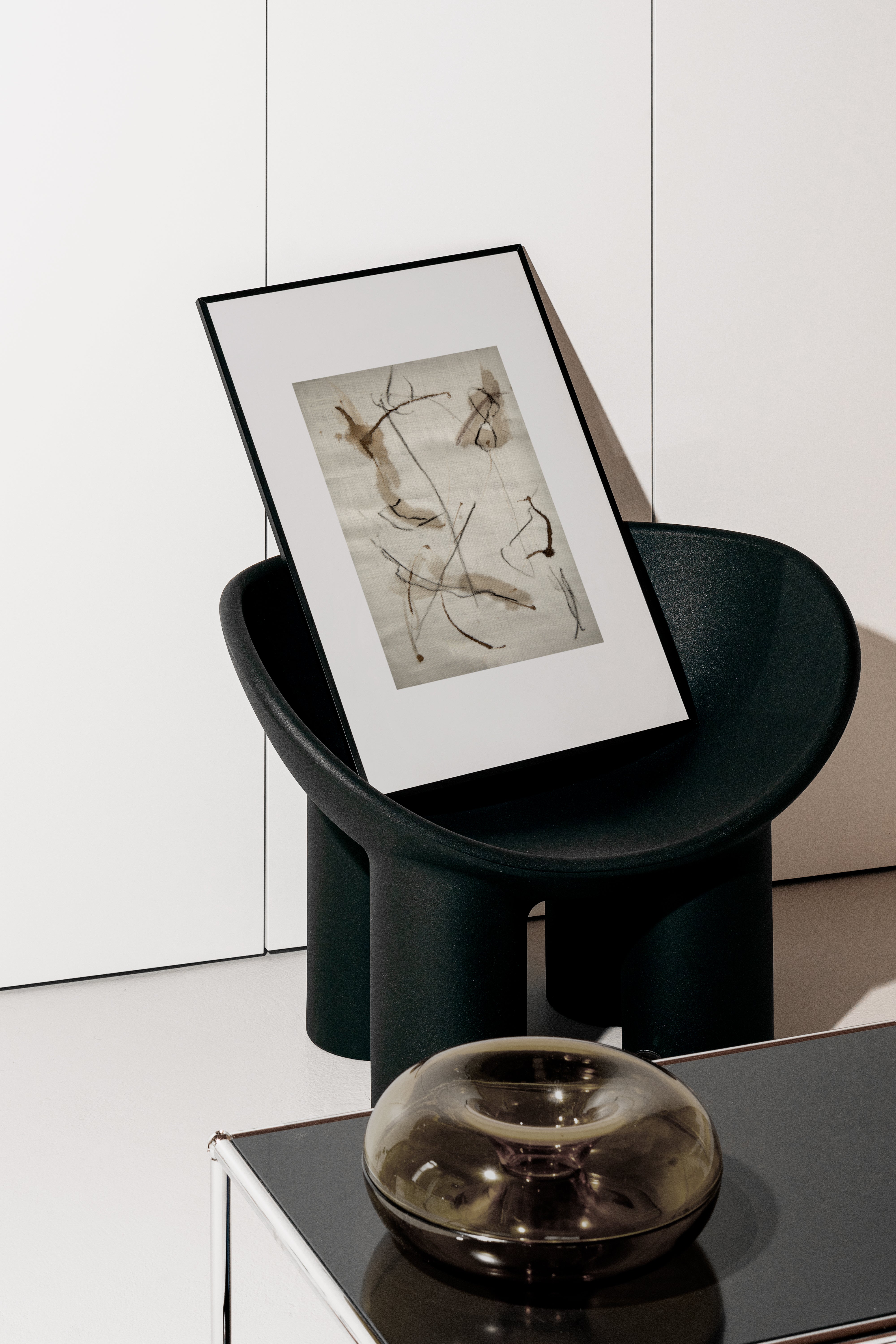 Black chair with a framed artwork and a metallic bowl on a white surface.